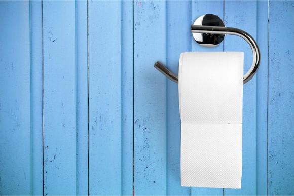 Toilet paper on holder attached to a light blue wall.