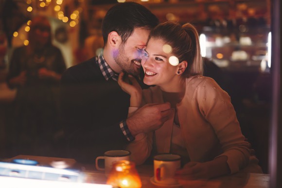 A man whispers into the ear of a smiling woman