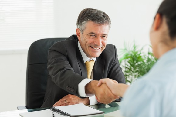Older man in a suit shaking hands with another professional