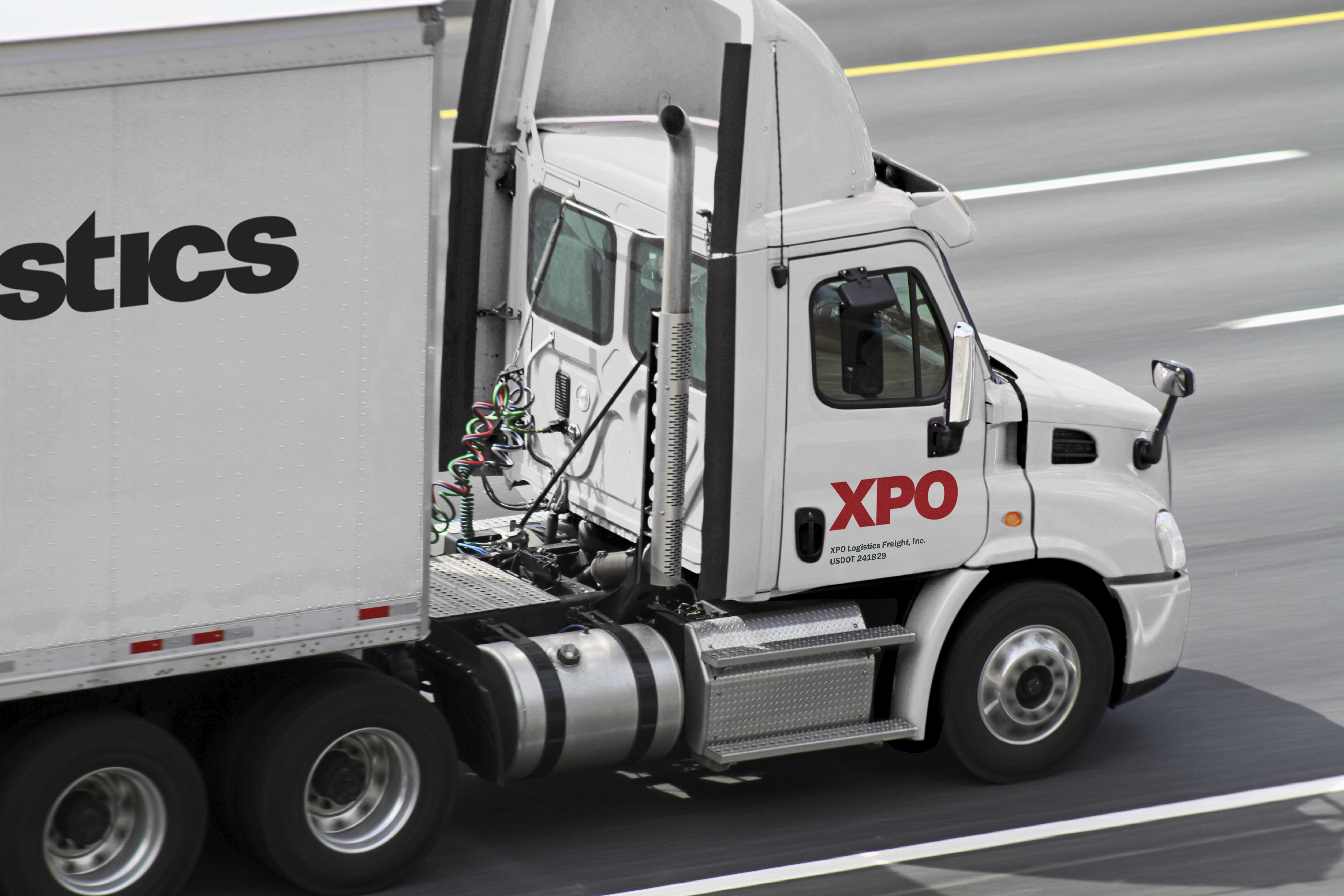 White semi tractor-trailer with XPO logo on it, driving down a four-lane highway.