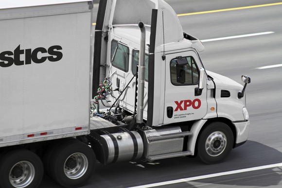 White semi tractor-trailer with XPO logo on it, driving down a four-lane highway.