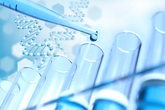 test tubes with a pipette dropping liquid in them and DNA strands in the background.