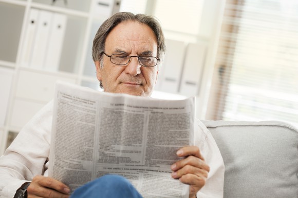 Older man on a sofa, reading a newspaper