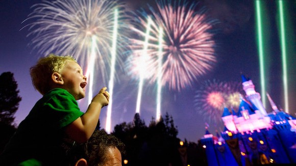 Young on the shoulder's on a man watching fireworks with a Disney Cinderella's Castle in background.