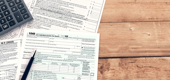 Tax forms with calculator and pen, spread out on a wooden surface.