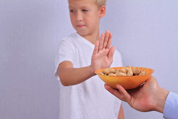 A child sticking their hand out to refuse a bowl of peanuts.