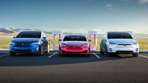 Three Tesla vehicles in blue, red, and white charging at a Supercharger location in daylight