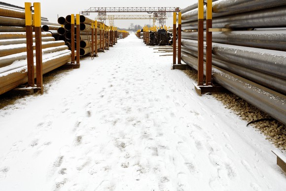 Neat stacks of pipes facing one another with snow on the ground in between