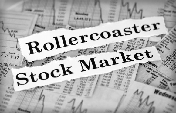 Pieces of paper with rollercoaster and stock market printed on them placed on top of newspaper stock charts and information