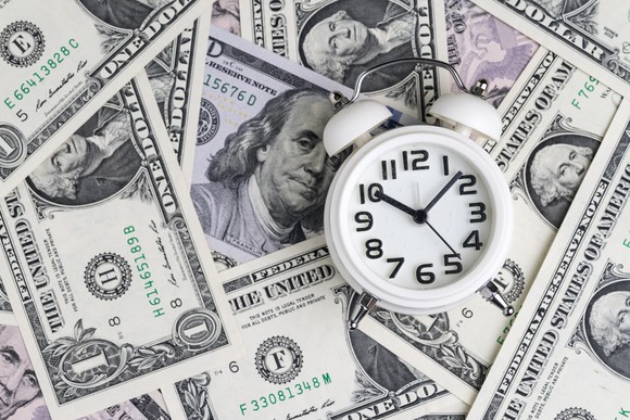 Alarm clock on pile of dollar bills