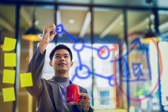 A man holding a coffee cup and drawing plans on a board.