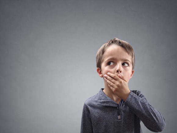 Blond child with grey shirt covering mouth, clearly thinking "oops"