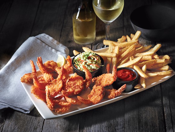 A shrimp entree from Applebee's on a table next to a small wine decanter, a glass of wine, and a napkin.