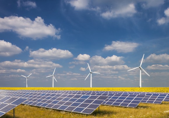 Solar farm in a field with wind turbines in the background.