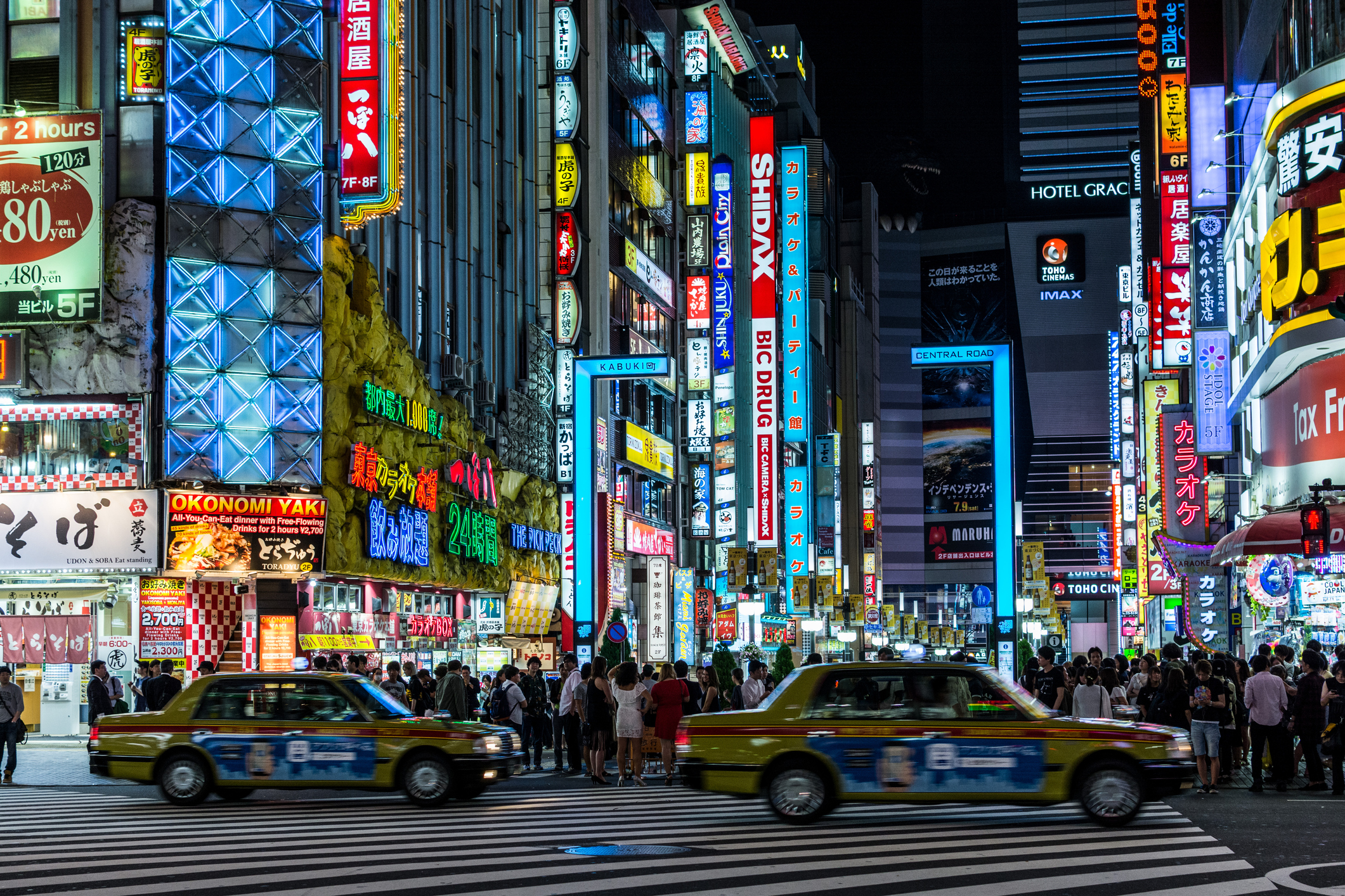 Two yellow Japanese taxis at nighttime, with buildings brightly lit in the background