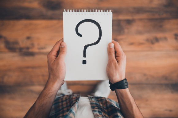 Man holding spiral notebook with question mark written on it
