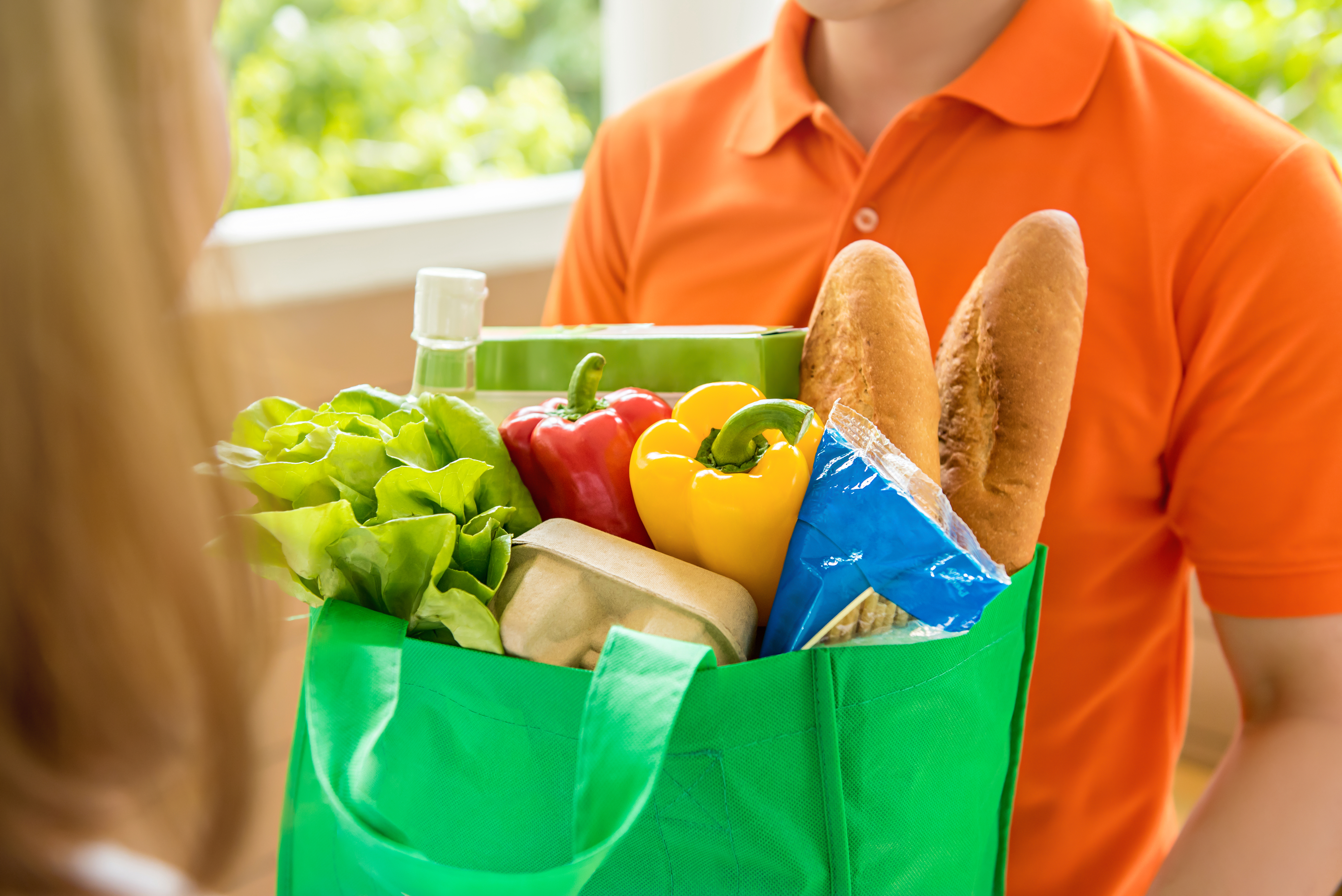 Person handing a bag of groceries to another person