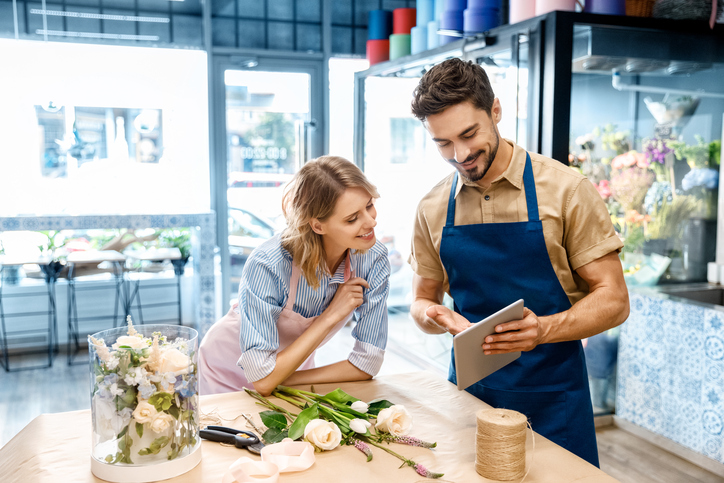 Two young florists using tablet device in their shop while putting together a flower arrangement.