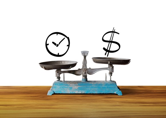 An old metal balance with a clock on one side and a dollar sign on the other side.