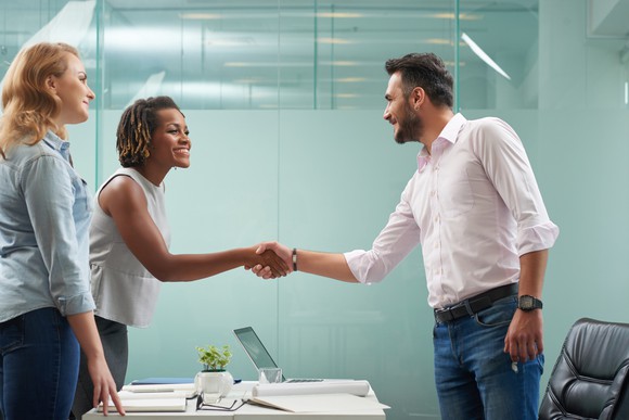 Two people shaking hands while a third looks on.