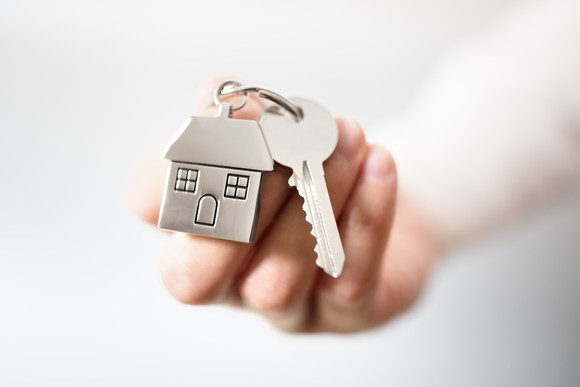 hand holding a key and a miniature house, both on a keyring.
