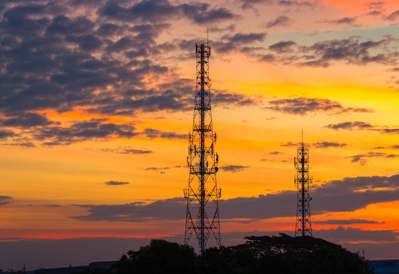 Cell towers with an orange sky and some clouds behind them.