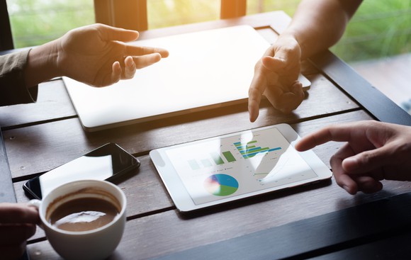 Tablet on table with people pointing at it.