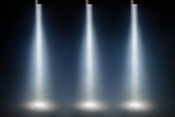 Three bright spotlights shining down on a dark stage.
