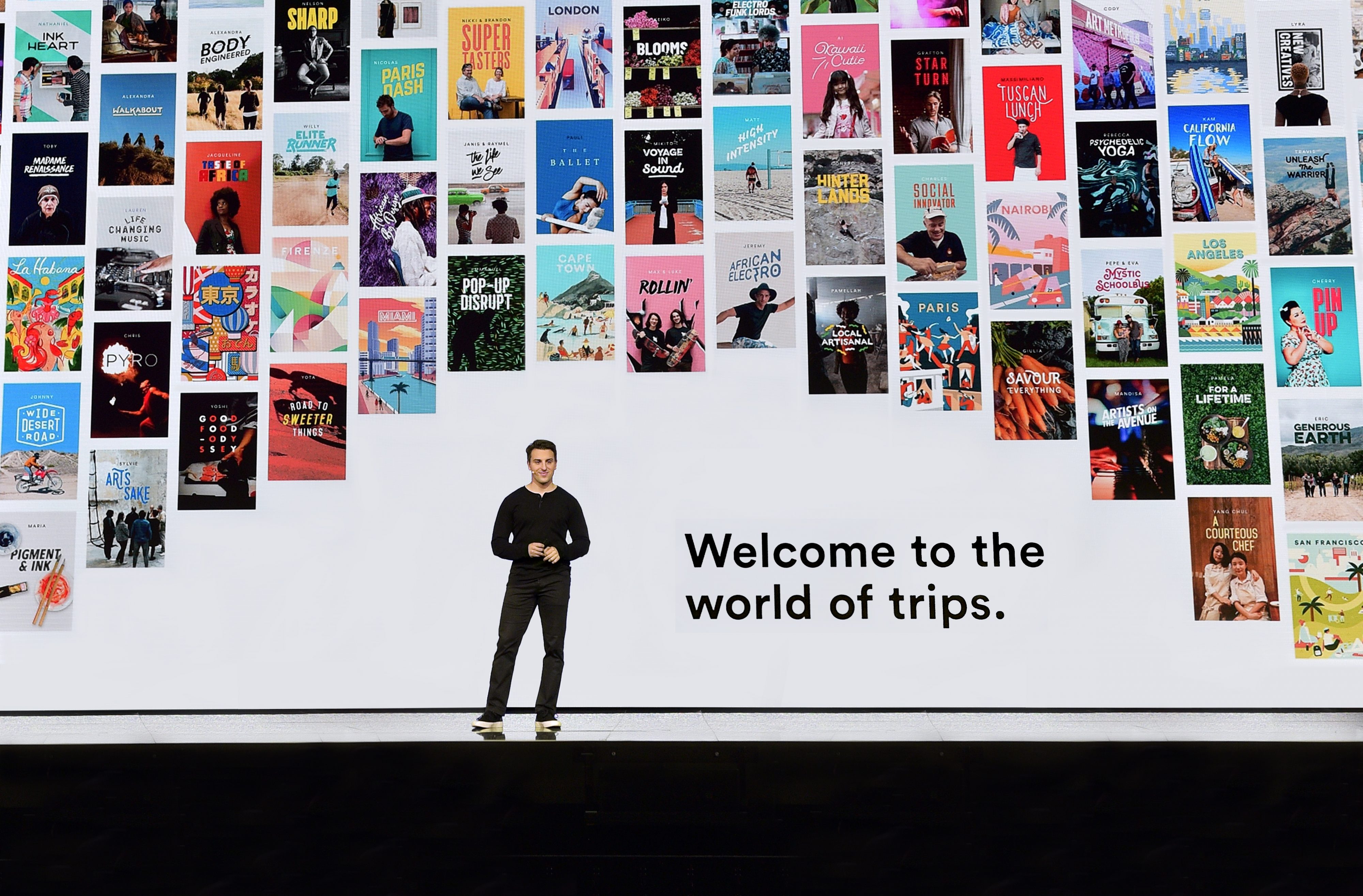 AirBnB CEO Brian Chesky speaks on stage in front of a backdrop that features Airbnb photos from around the world
