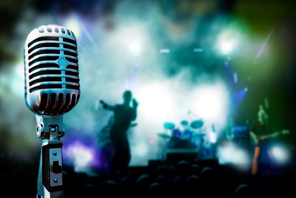Close-up view of a vintage microphone, with a live music show happening in the background.