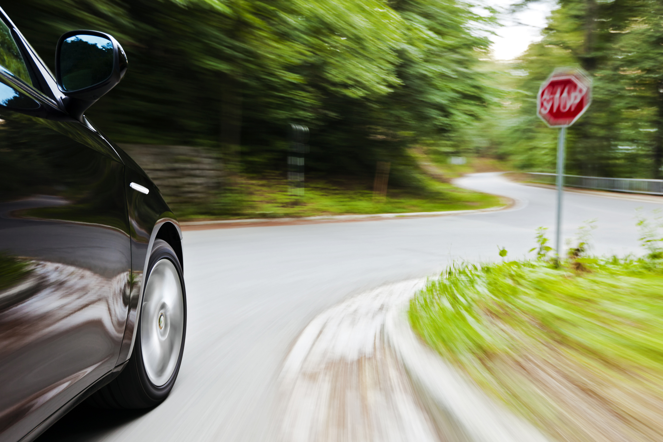 Front end of a car in motion nearing stop sign.