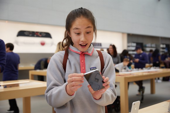 A girl with a surprised expression holds an iPhone in an Apple store.