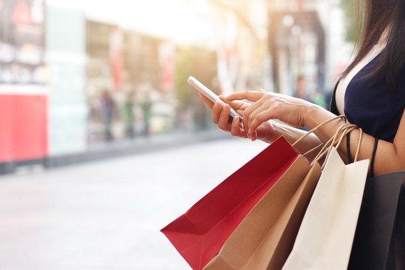 A woman holding several shopping bags on her arm as she types on her smartphone.