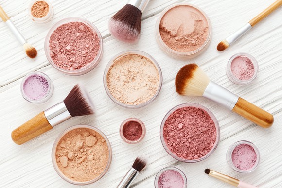 Makeup brushes and powders on white wooden table