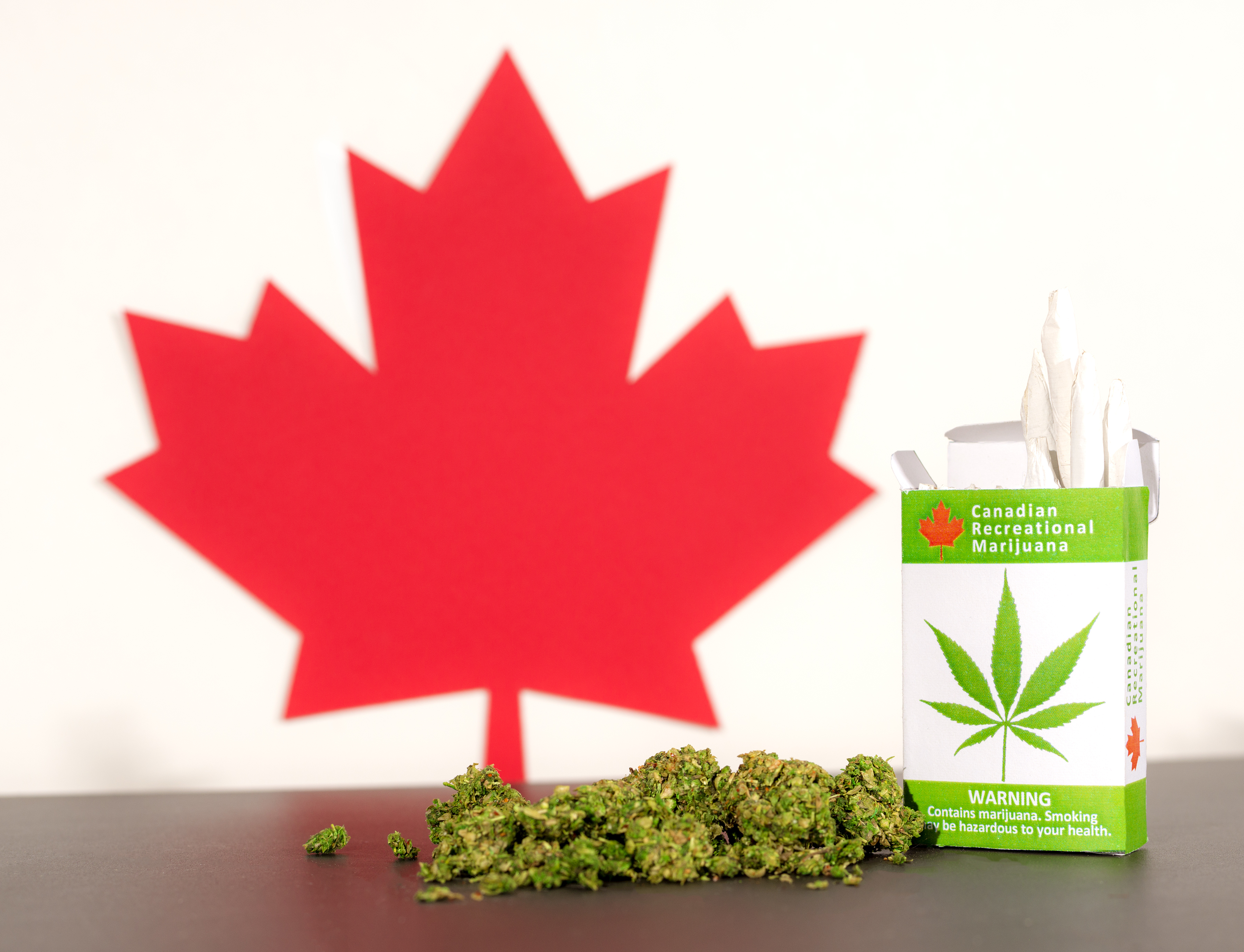 Canadian maple leaf next to marijuana buds and box of marijuana cigarettes