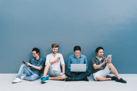 Millennials sitting on a floor using their electronic devices.