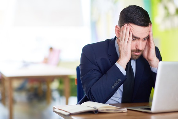 Man in suit at a computer, holding his head
