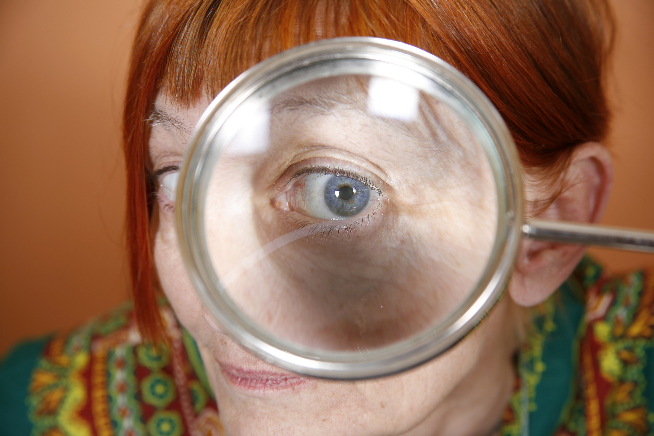A senior woman stares through a magnifying glass.