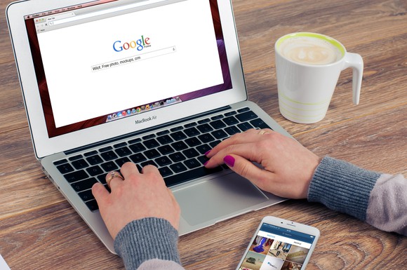 A person typing on a MacBook Air, with a coffee cup next to the MacBook Air and a smartphone near the touch pad.