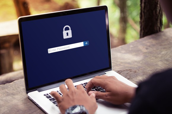 A person typing on a laptop with screen displaying a padlock icon and a password field