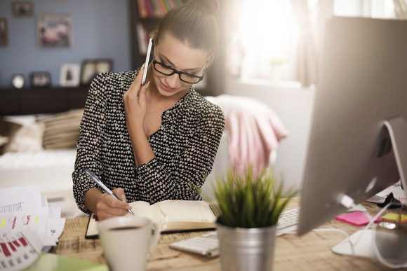Woman writing in a notebook while on the phone