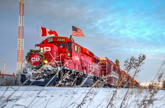 A red CP locomotive with the Canadian and U.S. flags on either side riding on a track with snow on the ground