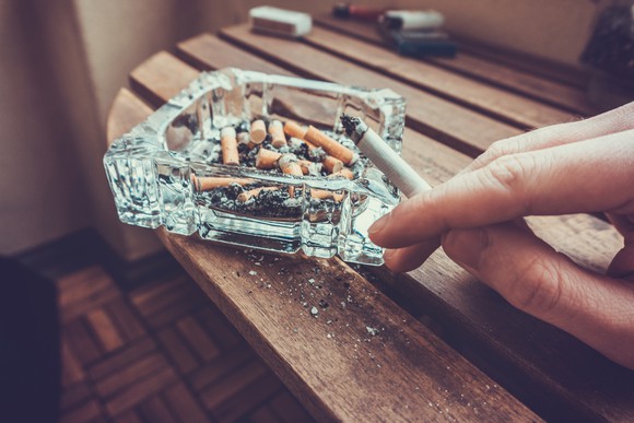 A person ashing a cigarette into an ashtray