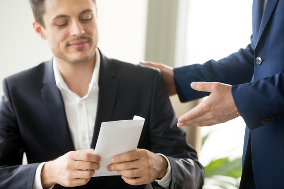 Man holding an envelope while another man pats him on the shoulder.