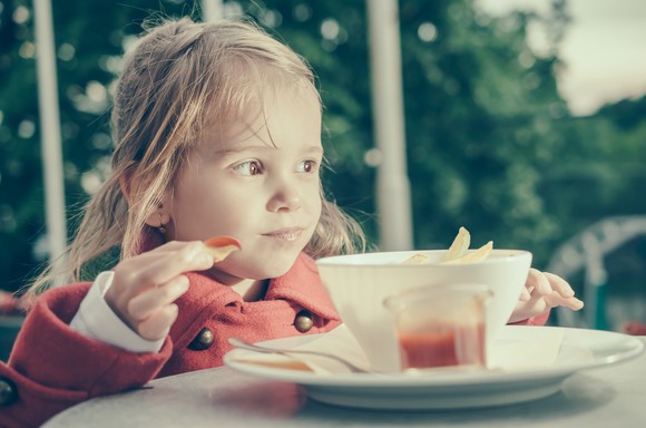 A little girl dipping fries in ketchup.