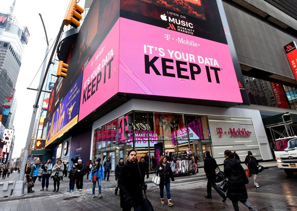 The outside of a T-Mobile store in Times Square, New York with people crossing the street in front of it.
