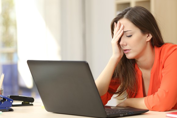 A woman puts her hand on her head while sitting at a laptop.