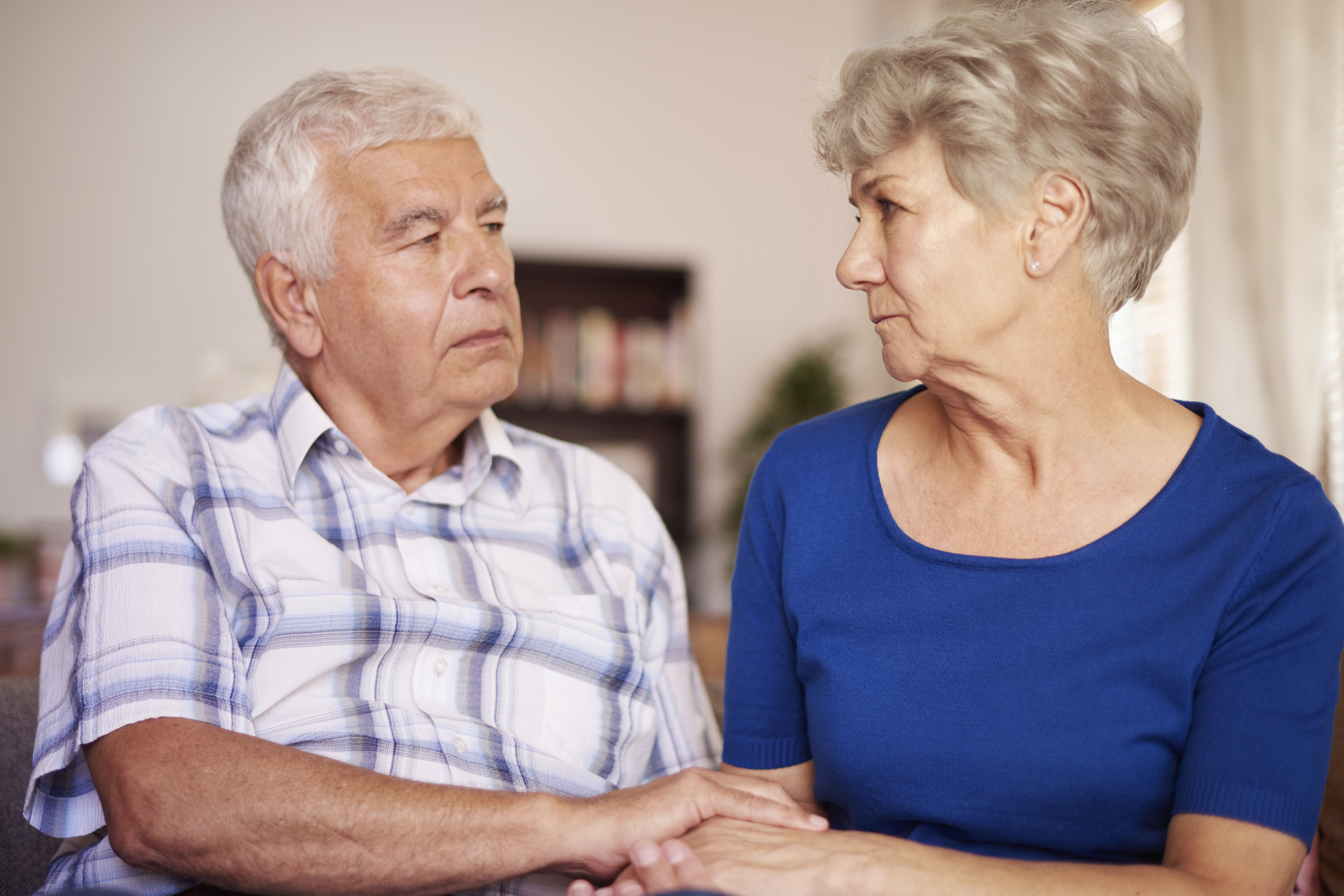 Senior man and woman holding hands and looking at each other with serious expressions