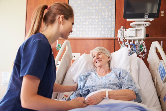 A nurse talking to a smiling senior female patient in a hospital bed.