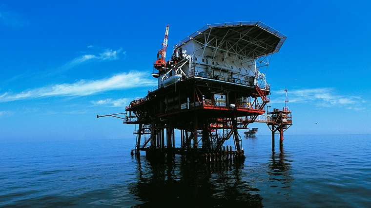 A drilling rig in the ocean with a blue sky in background.